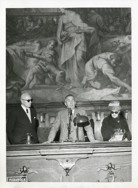 Convegno dell'Unione Italiana Ciechi - Interno - Tavolo della presidenza con relatori - Oratore al microfono, alla sua destra Eugenia Corno - Affresco della sala