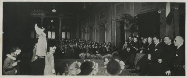 Istituto dei Ciechi di Milano - Sala Barozzi - Interno - Accademia in occasione della Messa d'oro di Monsignor Pietro Stoppani / Palco - Pietro Stoppani con i consiglieri e personale didattico dell'Istituto dei Ciechi - Bambini ciechi dell'Asilo Vitali cantano l'augurio a Monsignor Stoppani