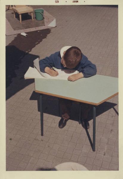 Istituto dei Ciechi di Milano - Scuola materna - Cortile - Bambino disegna seduto dietro a un tavolo - Grembiule
