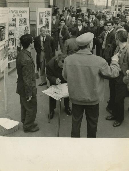 Milano - Stazione di Lambrate - Mostra fotografica e raccolta firme per il Vietnam - Uomo firma la petizione - Folla - Cartelli