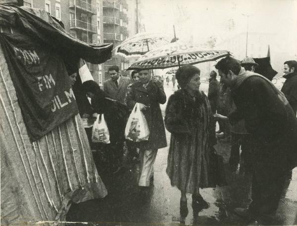 Milano - Viale Monza - Raccolta di firme per il Vietnam - Presidio in tenda - Cittadini firmano la petizione - Striscione Fiom Fim Uilm - Ombrelli