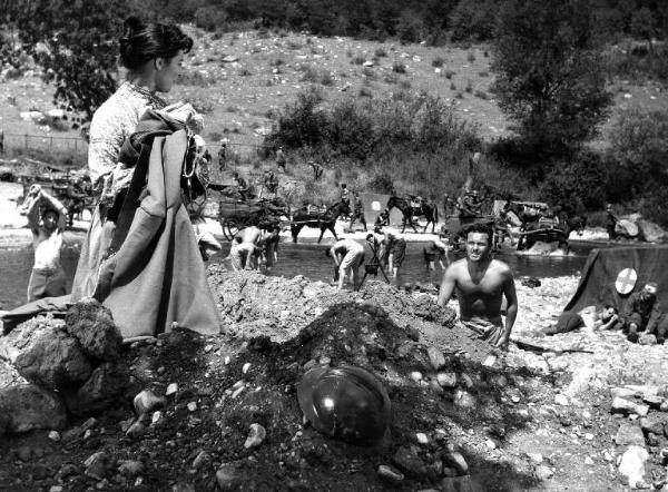 Scena del film "Il padrone sono me" - Regia Franco Brusati - 1955 - Due attori non identificati in primo piano, sullo sfondo gruppo di soldati al fiume