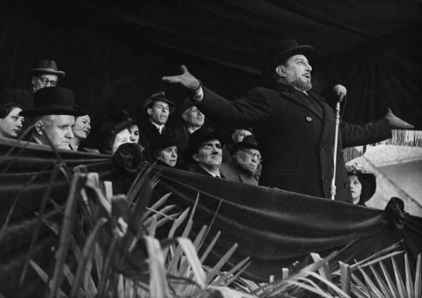 Scena del film "Il cappotto" - Regia Alberto Lattuada - 1952 - L'attore Giulio Stival al microfono su un palco. Dietro di lui un gruppo di attori non identificati