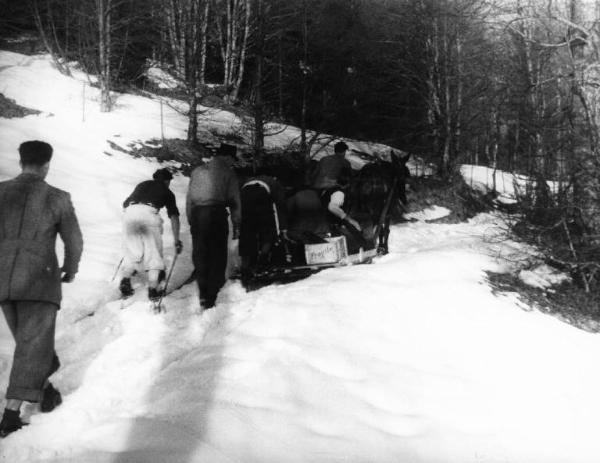 Set del film "Giacomo l'idealista" - Regia Alberto Lattuada - 1943 - Il regista Alberto Lattuada e alcuni operatori sulla neve trasportano gli attrezzi con su un carretto trainato da un asino