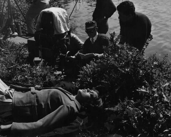 Set del film "I dolci inganni" - Regia Alberto Lattuada - 1960 - L'attrice Catherine Spaak stesa sul prato accanto al fiume con il regista Alberto Lattuada e gli operatori dietro la macchina da presa