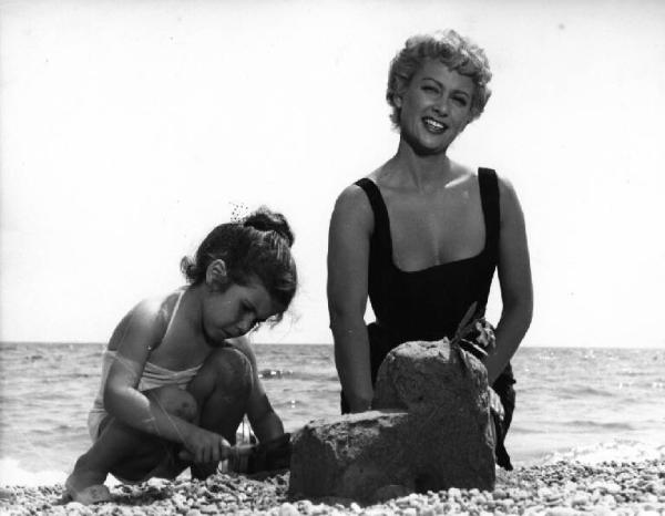 Scena del film "La spiaggia" - Regia Alberto Lattuada - 1953 - L'attrice Martine Carol con una bambina sulla spiaggia in riva al mare