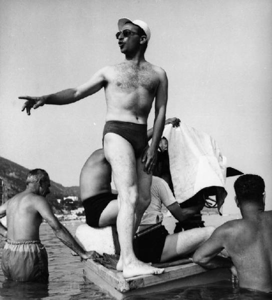 Set del film "La spiaggia" - Regia Alberto Lattuada - 1953 - Il regista Alberto Lattuada in costume su una pedana galleggiante sul mare con gli operatori della troupe