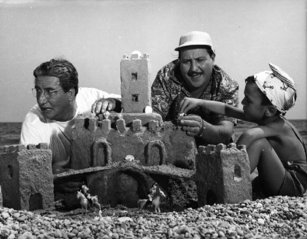 Scena del film "La spiaggia" - Regia Alberto Lattuada - 1953 - Gli attori Mario Carotenuto, Carlo Romano e un bambino costruiscon un castello di sabbia sulla spiaggia