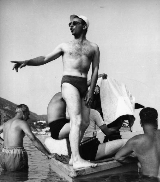 Set del film "La spiaggia" - Regia Alberto Lattuada - 1953 - Il regista Alberto Lattuada in costume su una pedana galleggiante sul mare con gli operatori della troupe