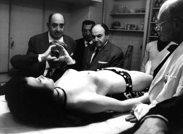 Set del film "Don Giovanni in Sicilia" - Regia Alberto Lattuada - 1967 - Il regista Alberto Lattuada e gli operatori della troupe osservano il manichino di una donna nuda stesa sul tavolo