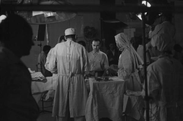 Set del film "Anna" - Regia Alberto Lattuada - 1951 - L'attrice Silvana Mangano in abito da suora infermiera con il regista Alberto Lattuada sul set con altri infermieri e gli operatori della troupe