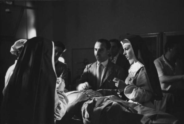 Set del film "Anna" - Regia Alberto Lattuada - 1951 - L'attrice Silvana Mangano in abito da suora infermiera con il regista Alberto Lattuada sul set con altri infermieri e gli operatori della troupe