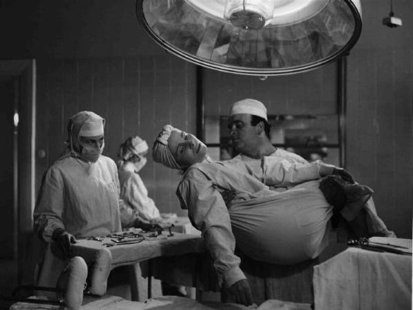 Scena del film "Anna" - Regia Alberto Lattuada - 1951 - L'attore Mimmo Poli, in camice bianco da infermiere, in ospedale tiene tra le braccia una paziente