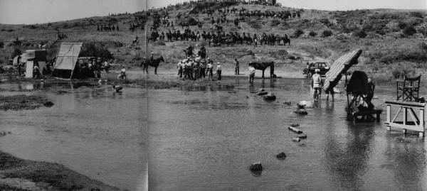 Set del film "Attila" - Regia Pietro Francisci - 1954 - Operatori della troupe ai bordi di un fiume per riprendere una scena con attori a cavallo su una collina