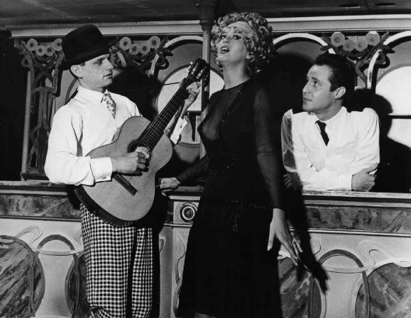 Scena del film "Aveva due pistole con gli occhi bianchi e neri" - Regia Dario Fo - 1960 - L'attore Dario Fo con una chitarra in mano e due attori non identificati