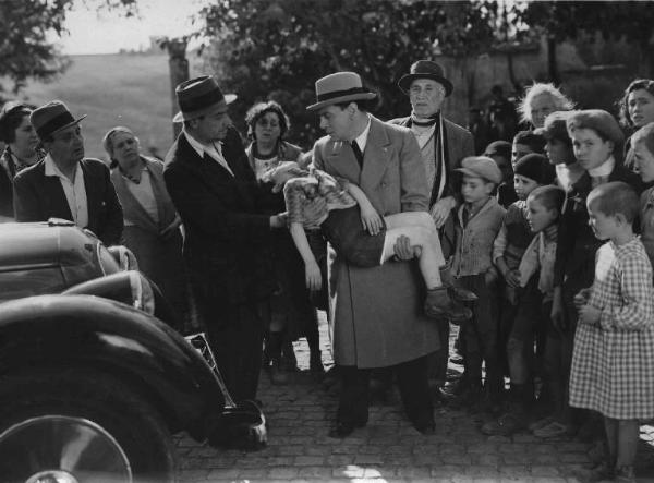 Scena del film "Chi è più felice di me?" - Regia Guido Brignone - 1938 - L'attore Tito Schipa con un bambino in braccio con un gruppo di attori non identificati.