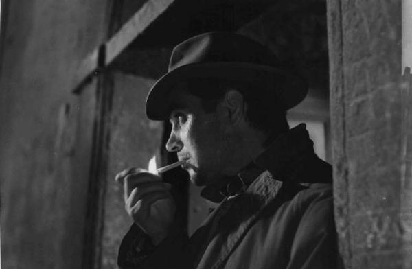 Scena del film "La città si difende" - Regia Pietro Germi - 1951 - L'attore Renato Baldini fuma una sigaretta appoggiato al muro