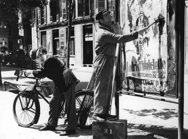 Scena del film "Come scopersi l'America" - Regia Carlo Borghesio - 1949 - Un attore non identificato osserva l'attore Erminio Macario mentre attacca un manifesto