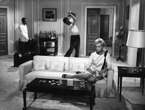 Scena del film "Copacabana Palace" - Regia Steno - 1962 - L'attore Cyll Farney gioca a golf in salotto, mentre l'attrice Mylène Demongeot siede sul divano, fumando una sigaretta