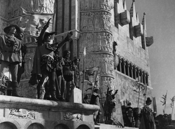 Set del film "La corona di ferro" - Regia Alessandro Blasetti - 1940 - Un gruppo di attori non identificati in piedi davanti ad un palazzo.
