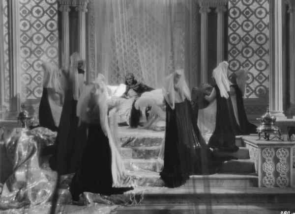 Set del film "La corona di ferro" - Regia Alessandro Blasetti - 1940 - L'attrice Elisa Cegani su un letto sfarzoso circondata da attrici non identificate.
