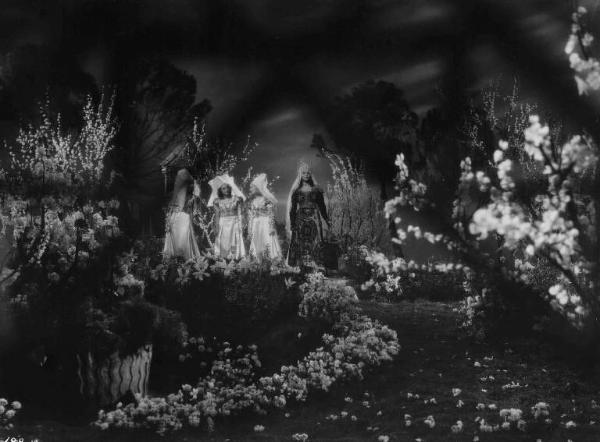 Set del film "La corona di ferro" - Regia Alessandro Blasetti - 1940 - L'attrice Luisa Ferida in abiti regali in un bosco fiorito con alcune attrici non identificate.