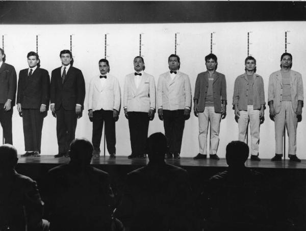 Set del film "Crimen" - Regia Mario Camerini- 1960 - L'attore Vittorio Gassman, l'attore Alberto Sordie l'attore Nino Manfredi insieme ad altri attori nonidentificati in fila per delle foto segnaletiche.