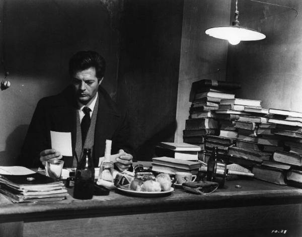 Set del film "Cronaca familiare" - Regia Valerio Zurlini 1962 - L'attore Marcello Mastroianni guarda fotografie seduto ad una scrivania.