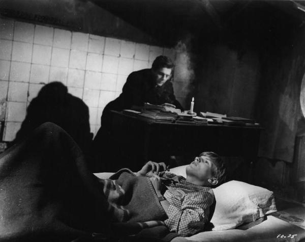 Set del film "Cronaca familiare" - Regia Valerio Zurlini 1962 - L'attore Jacques Perrin sdraiato su un letto in primo piano con alle spalle l'attore Marcello Mastroianni seduto alla scrivania.