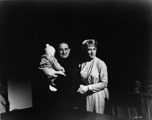 Set del film "Cronaca familiare" - Regia Valerio Zurlini 1962 - L'attore Salvo Randone con in braccio un bambino piccolo sta accanto ad un'attrice non identificata in un interno buio.