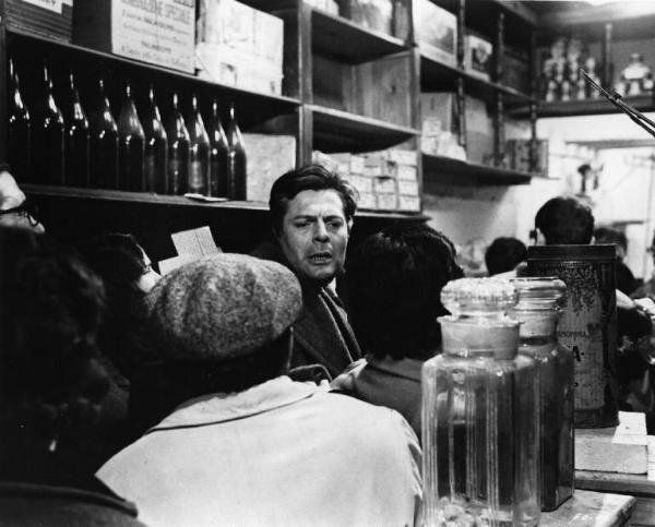 Set del film "Cronaca familiare" - Regia Valerio Zurlini 1962 - L'attore Marcello Mastroianni si fa largo in una dispensa affollata.