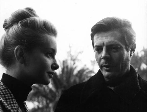 Set del film "Cronaca familiare" - Regia Valerio Zurlini 1962 - L'attrice Valeria Ciangottini e l'attore Marcello Mastroianni conversano in primo piano all'aperto.