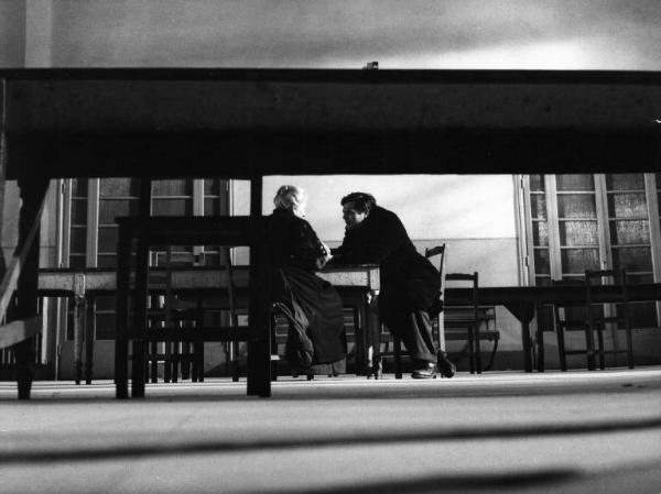 Set del film "Cronaca familiare" - Regia Valerio Zurlini 1962 - L'attore Marcello Mastroianni e una donna anziana di spalle conversano seduti ad un tavolo in una grande sala.
