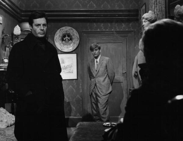 Set del film "Cronaca familiare" - Regia Valerio Zurlini 1962 - Gli attori Marcello Mastroianni e Jacques Perrin con un uomo di spalle in un interno.
