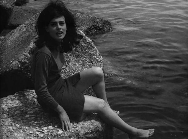 Fotografia del film "La cuccagna" - Regia Luciano Salce 1962 - L'attrice Donatella Turri seduta su uno scoglio bagna i piedi in acqua.