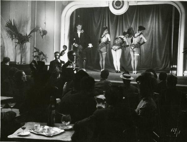 Scena del film "Il delitto di Giovanni Episcopo" - Regia Alberto Lattuada, 1947 - Teatro di varietà, sul palco, il presentatore guarda il fondo schiena delle ballerine, in costume di scena.