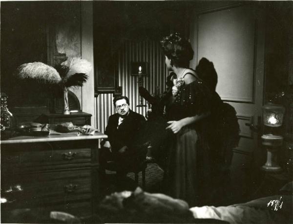 Scena del film "Il delitto di Giovanni Episcopo" - Regia Alberto Lattuada, 1947 - Sullo sfondo, Aldo Fabrizi è seduto e guarda Yvonne Sanson, in primo piano, in piedi. Lei guarda verso di lui e tiene in mano un candelabro.