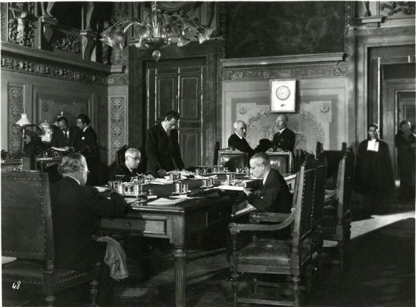 Scena del film "Il delitto di Giovanni Episcopo" - Regia Alberto Lattuada, 1947 - Totale. Al centro della stanza, un grande tavolo con impiegati seduti che lavorano. In piedi, Roldano Lupi legge un foglio appoggiato sul tavolo.