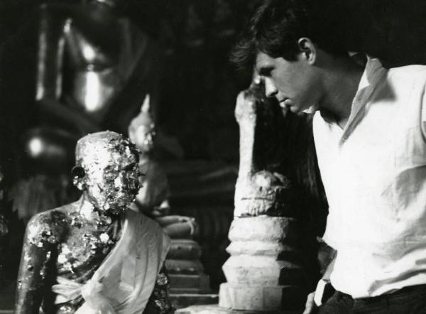 Scena del film "La diga sul Pacifico" - Regia René Clément, 1957 - Mezza figura di profilo di Anthony Perkins mentre guarda una statua con evidenti tracce di corrosione.