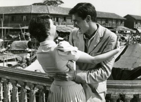 Scena del film "La diga sul Pacifico" - Regia René Clément, 1957 - Mezza figura di Silvana Mangano e Anthony Perkins su una terrazza mentre si abbracciano e ridono. Lei lo tiene per le spalle, lui per la vita.