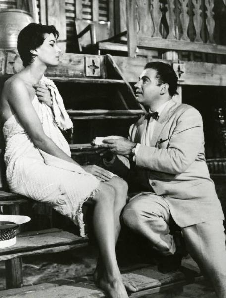 Scena del film "La diga sul Pacifico" - Regia René Clément, 1957 - Su una scalinata di legno Silvana Mangano, avvolta in un asciugamano con la pelle bagnata, siede e parla con Nehemiah Persoff, seduto più in basso, che le porge qualcosa.