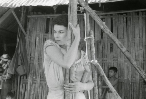 Scena del film "La diga sul Pacifico" - Regia René Clément, 1957 - Mezza figura di Silvana Mangano abbracciata a un palo di legno. Sullo sfondo bambini di origini asiatiche e un attore non identificato.