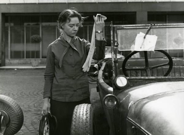 Scena del film "La diga sul Pacifico" - Regia René Clément, 1957 - Piano americano di Jo Van Fleet in piedi di fianco a un'automobile. L'attrice regge una borsa nella mano destra e osserva un guanto da donna che regge con la mano sinistra.