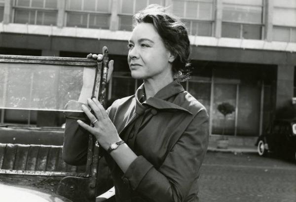 Scena del film "La diga sul Pacifico" - Regia René Clément, 1957 - Mezza figura di Jo Van Fleet accanto a un'automobile. L'attrice appoggia le mani sul parabrezza e guarda verso destra.