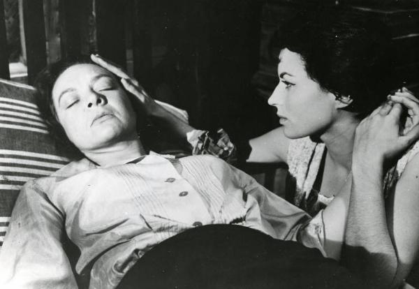 Scena del film "La diga sul Pacifico" - Regia René Clément, 1957 - Jo Van Fleet è sdraiata su un letto con gli occhi chiusi. Al suo fianco, accovacciata, Silvana Mangano le accarezza la testa con la mano destra e con la sinistra le tiene la mano.