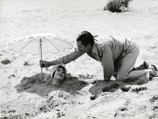 Scena del film "Divorzio all'italiana" - Regia Pietro Germi, 1961 - In spiaggia Marcello Mastroianni sistema un ombrellino vicino alla testa di Daniela Rocca. L'attrice ha il resto del corpo completamente coperto di sabbia.