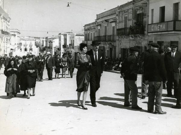 Scena del film "Divorzio all'italiana" - Regia Pietro Germi, 1961 - Daniela Rocca e Marcello Mastroianni passeggiano a braccetto per il paese in mezzo ad altre persone.