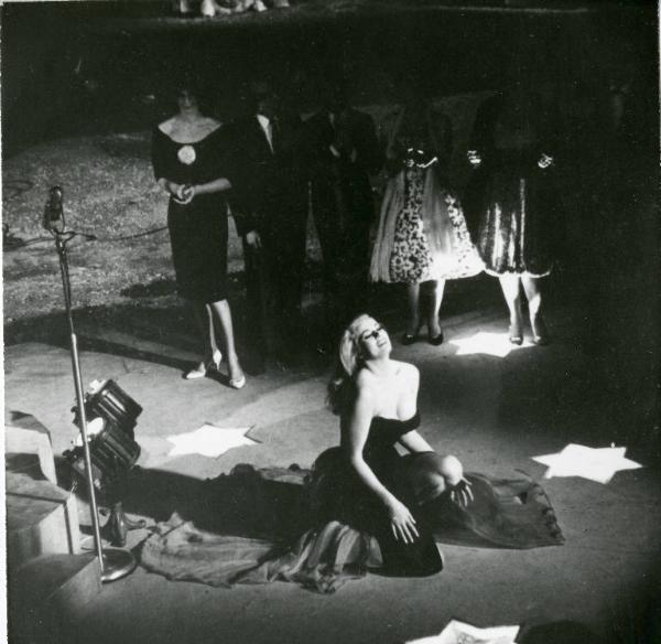 Scena del film "La dolce vita" - Regia Federico Fellini, 1960 - Totale in plongé di Anita Ekberg, di profilo, appoggiata su un ginocchio. Alcune figure femminili, alle sue spalle, in semioscurità, la osservano.