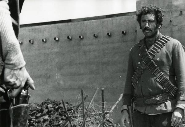 Scena del film "Un dollaro tra i denti" - Regia Luigi Vanzi, 1966 - Piano americano di Frank Wolff mentre fissa la mano di un pistolero che impugna l'arma nella fondina, inquadrata in dettaglio.