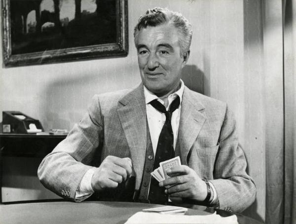 Scena del film "Domenica è sempre domenica" - Regia Camillo Mastrocinque, 1958 - Mezza figura frontale di Vittorio De Sica, seduto a un tavolo rotondo. L'attore ha in mano delle carte.